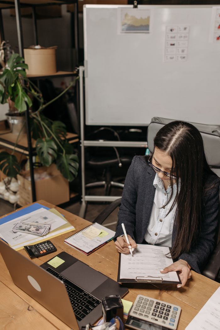 Businesswoman focused on accounting tasks, writing on a clipboard at a modern office desk.